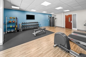 Academia com equipamentos de ginástica, uma TV na parede e uma porta com janela.