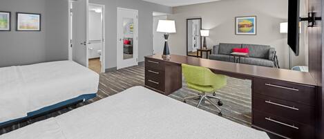 A hotel room with two beds, a desk, a chair, a TV, and a bathroom visible through an open door.