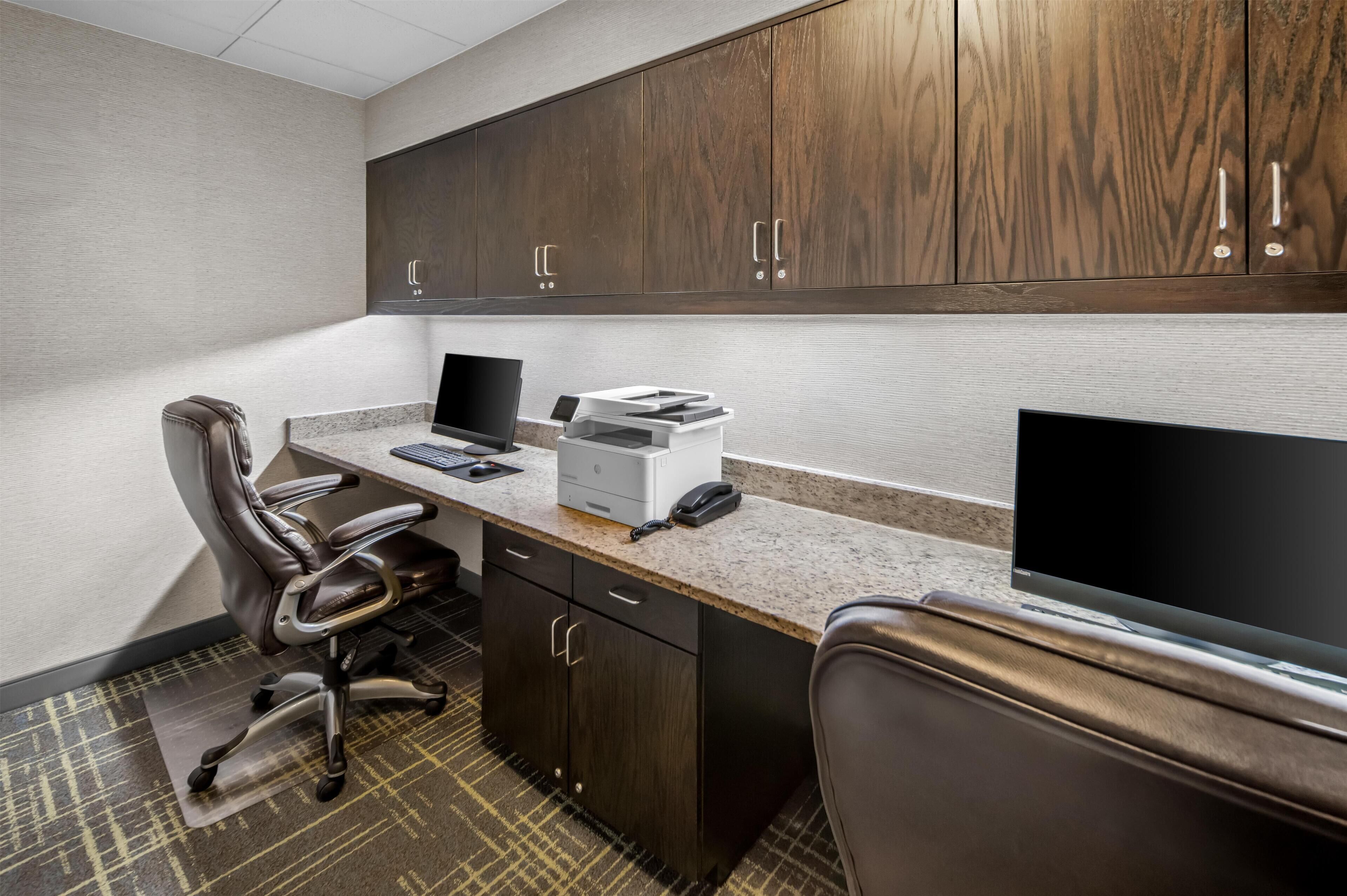 A modern office space with a desk, chair, computer, printer, and cabinets.