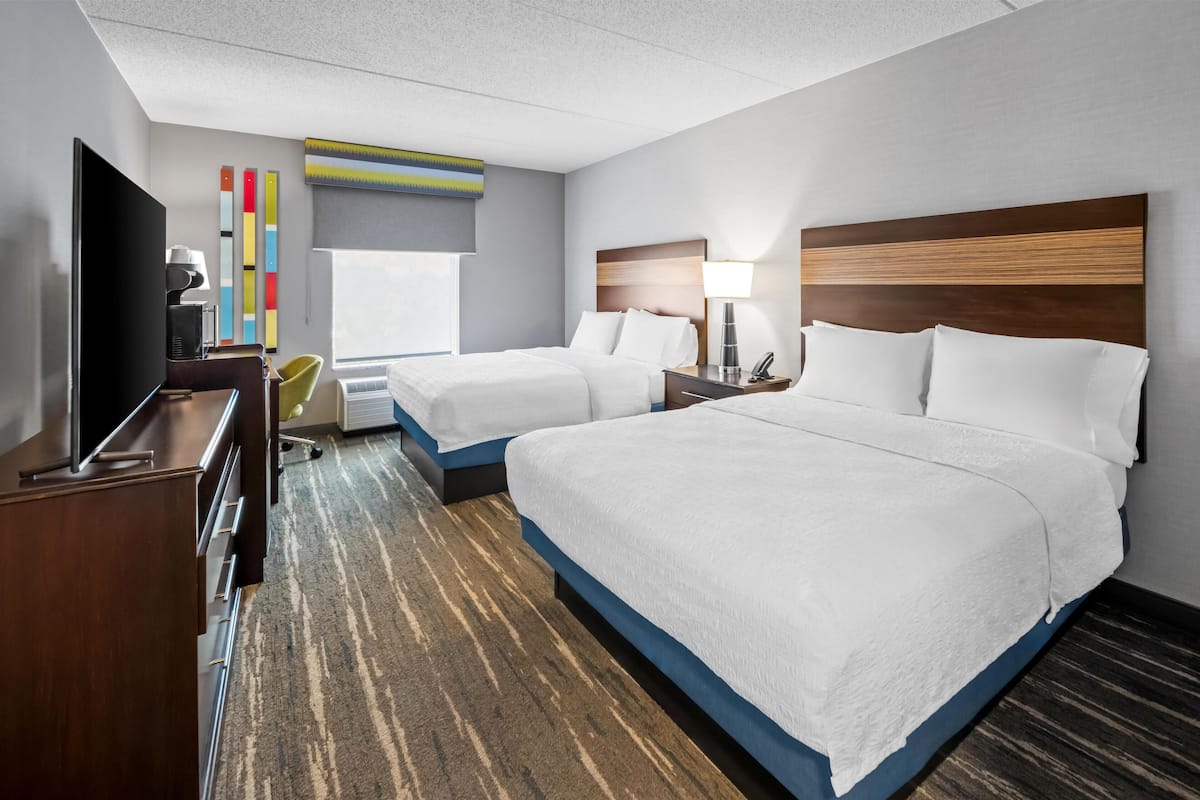 A hotel room with two beds, a TV, a desk, and a chair.