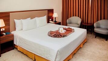 A neatly made bed with a white and brown bedspread, a bedside lamp, a phone, and a small table with a lamp.