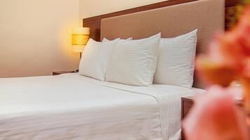 A neatly made bed with white linens and pillows, a wooden headboard, and a bedside lamp.