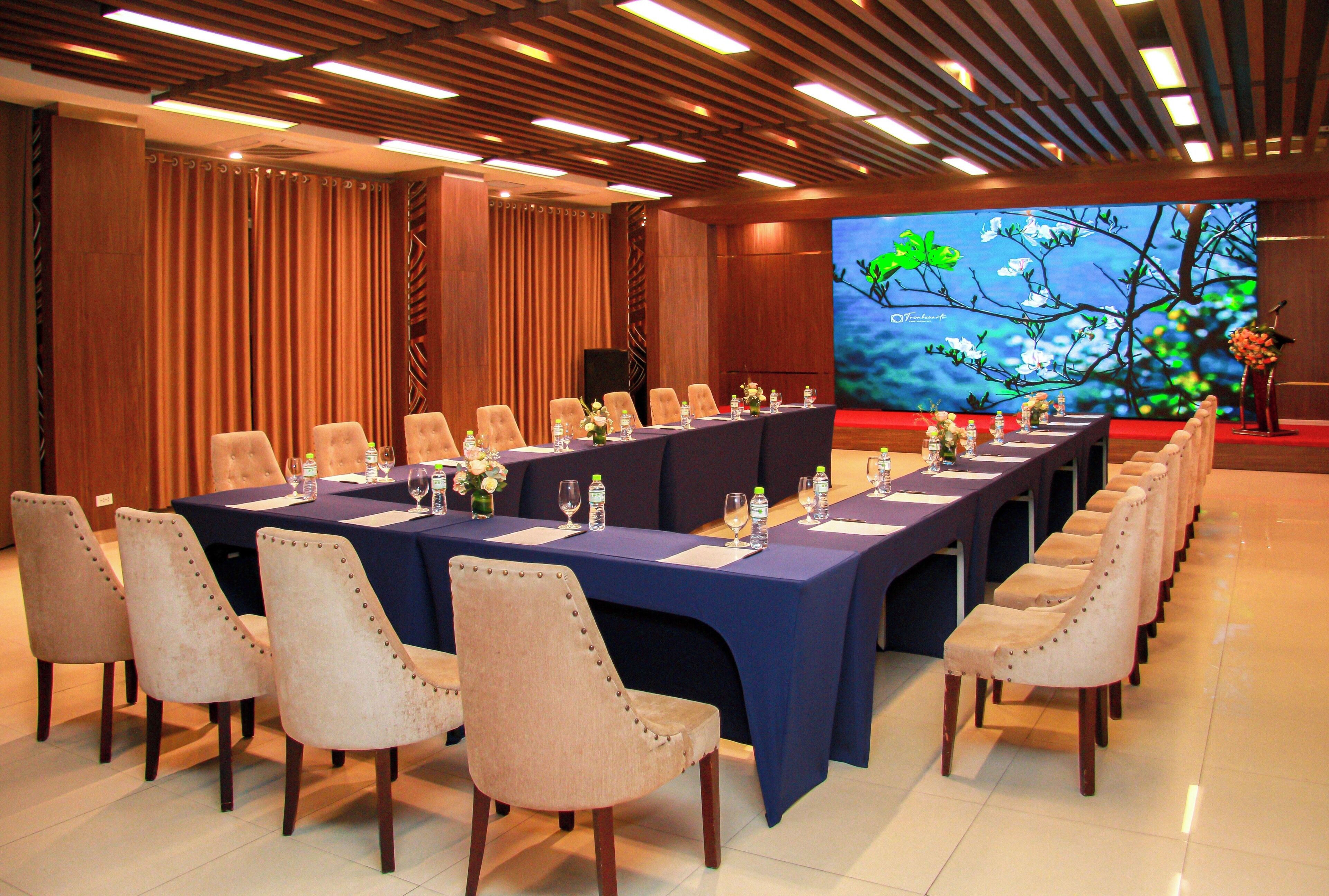 A conference room with a long table, multiple chairs, and a large screen displaying a nature scene.