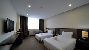 Ett hotellrum med två sängar, ett skrivbord, en stol, en TV och ett fönster med gardiner.