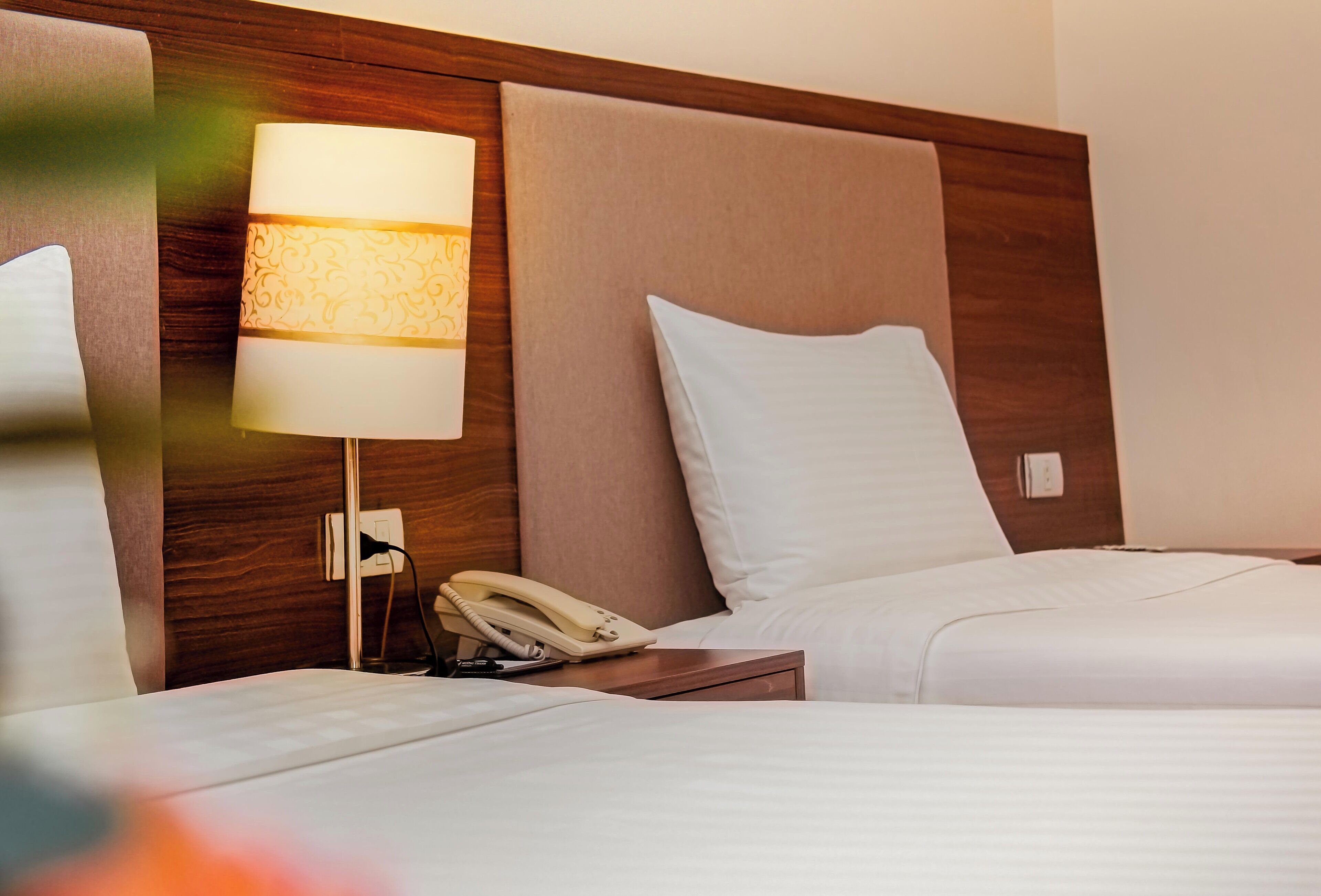 A hotel room with two beds, a bedside lamp, a telephone, and a wooden headboard.