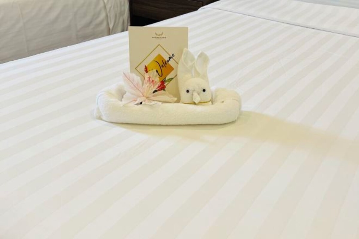 Una cama bien hecha con un edredón blanco y una tarjeta de bienvenida sobre una almohada.