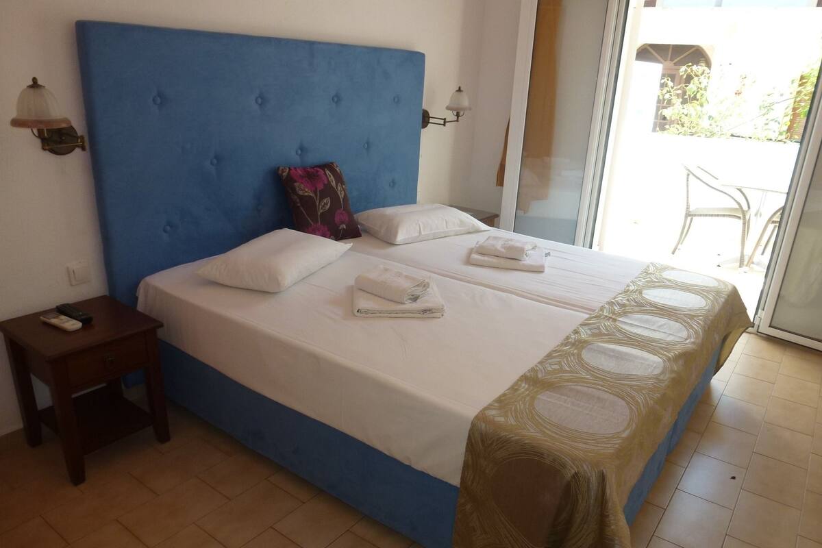A hotel room with a large bed, a small bedside table, and a view of the outside.