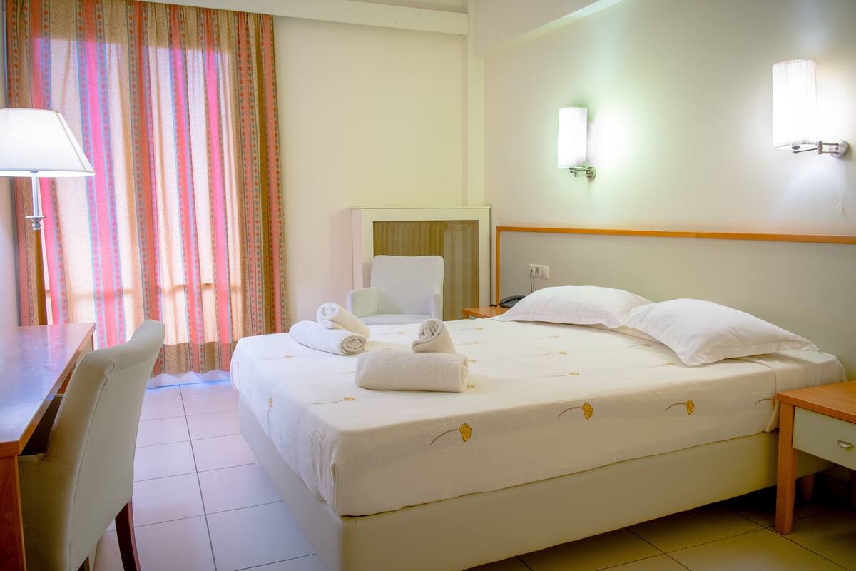 Una habitación de hotel con cama, escritorio, silla, espejo y lámpara.