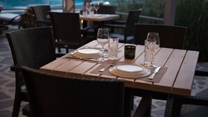 Ein Esstisch für zwei Personen, gedeckt mit Geschirr, Besteck und Gläsern, mit Blick auf einen Poolbereich.