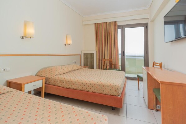 A hotel room with a bed, a desk, a chair, a TV, and a window with curtains.