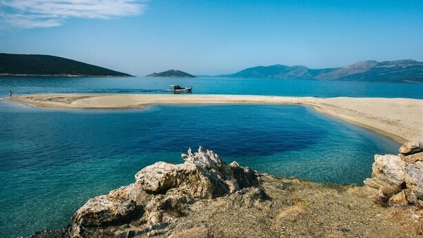 Eine Küstenlandschaft mit klarem, blauem Wasser, einem Sandstrand und Felsformationen.