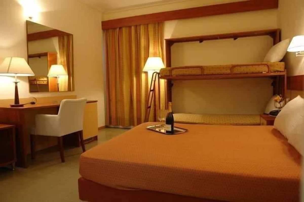 Habitación de hotel con literas, un escritorio, una silla, una lámpara y un espejo.