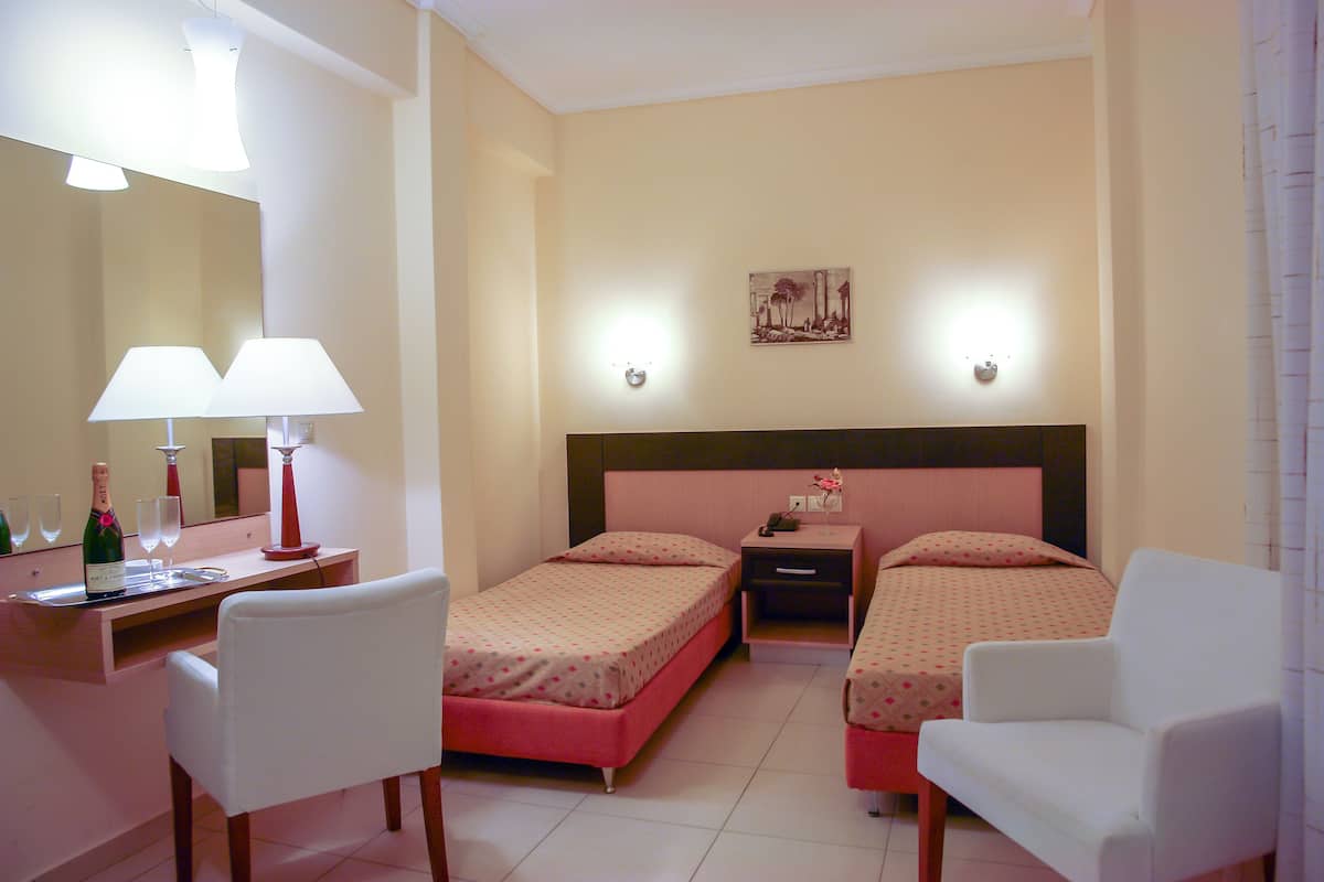 Habitación de hotel con dos camas, un escritorio con silla, un espejo y dos mesitas de noche con lámparas.