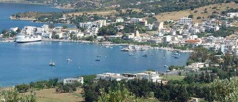 A coastal town with a marina, buildings, and hills in the background.