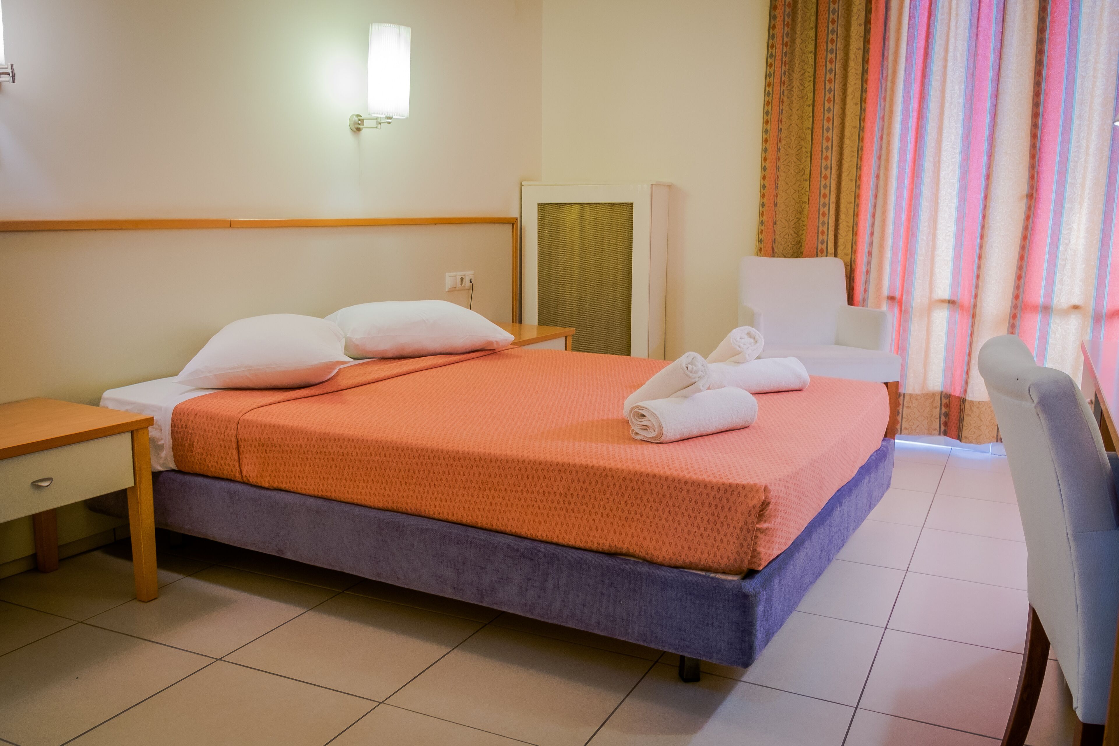Una habitación de hotel con cama, escritorio, silla, espejo y ventana con cortinas.