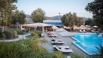 A poolside area with lounge chairs and umbrellas, a children's play area, and a building with a blue roof.