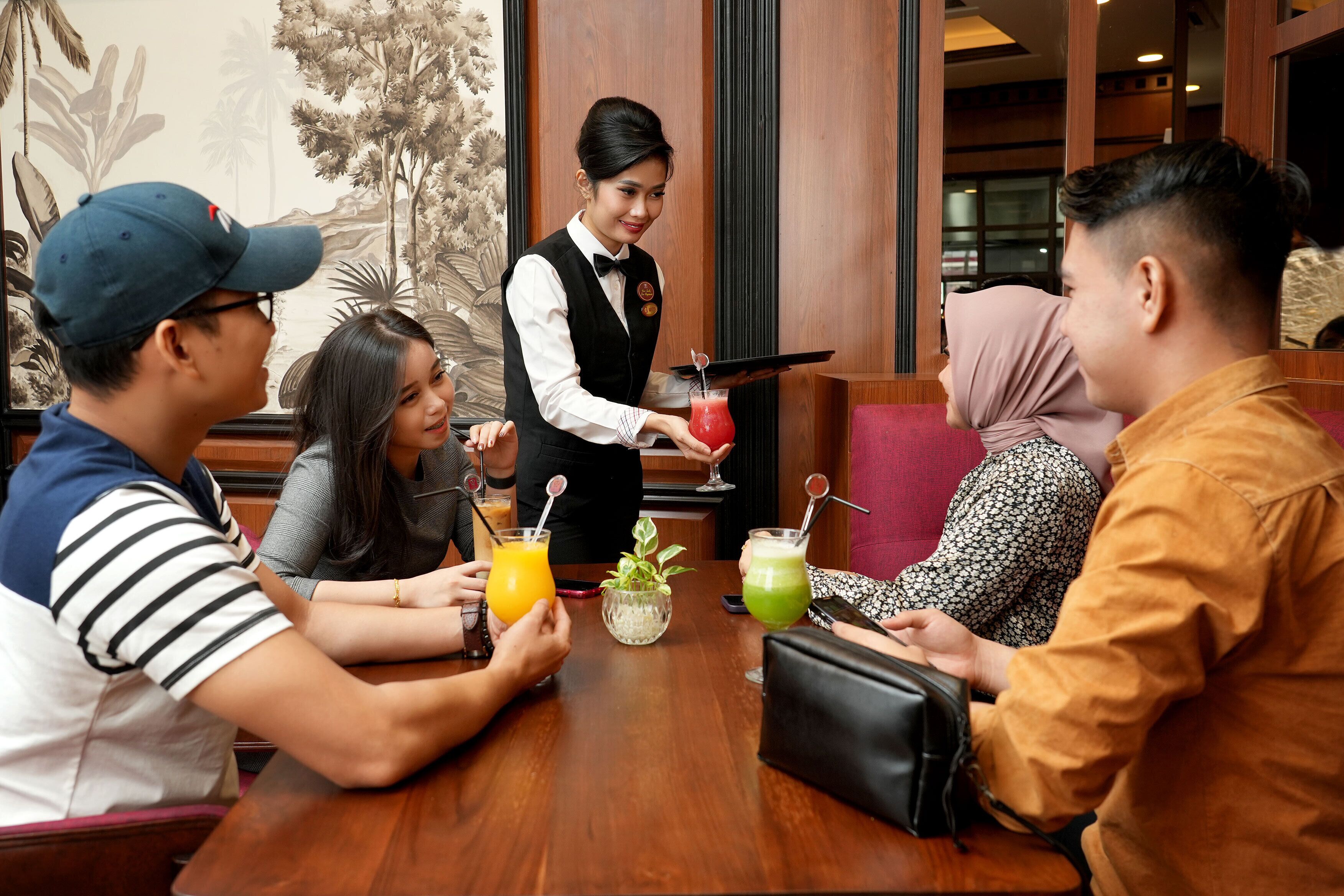 A group of people seated at a wooden table in a restaurant with a waiter serving drinks.