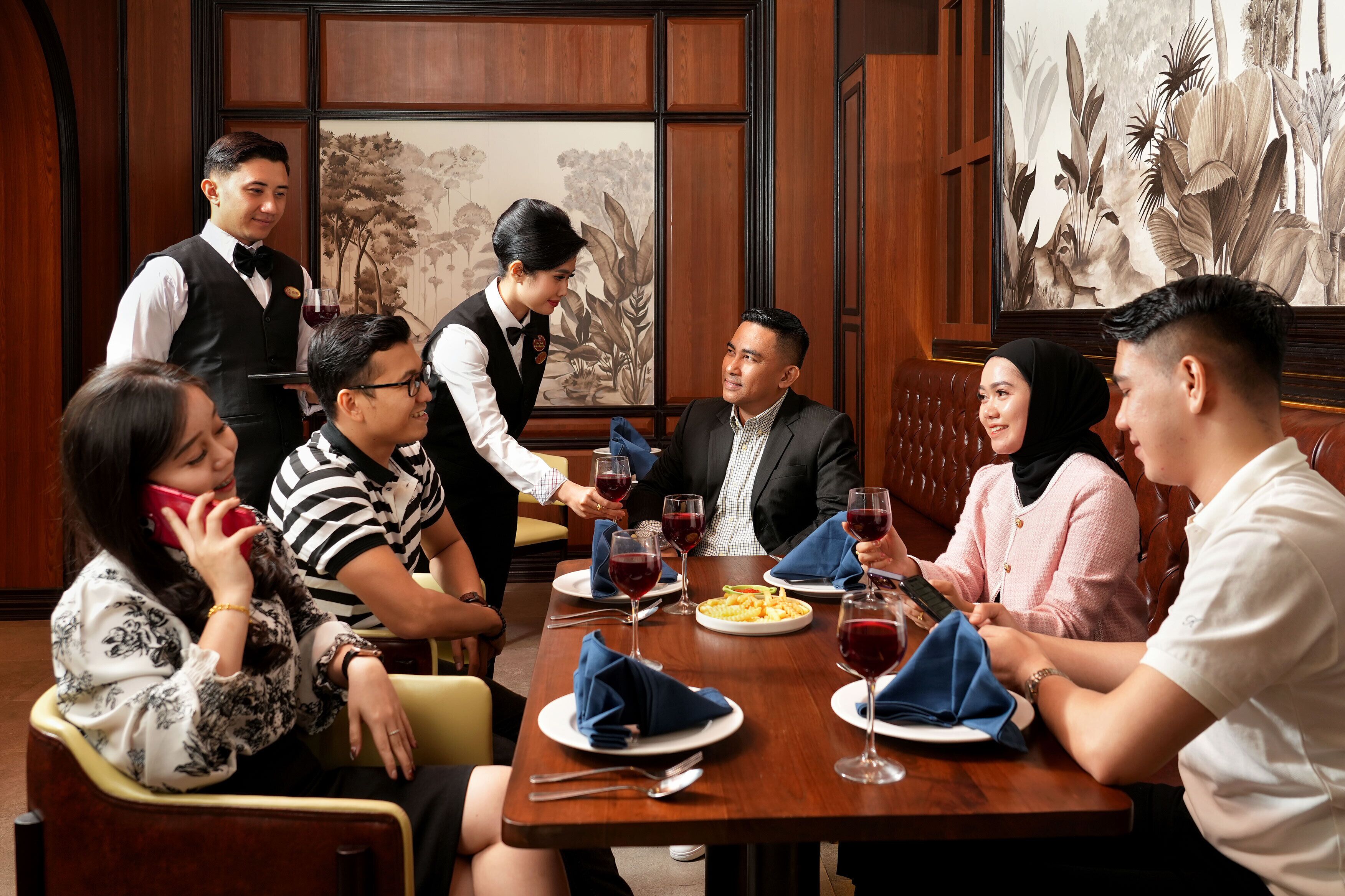 A group of people dining in a restaurant with wooden paneling and a large floral painting on the wall.