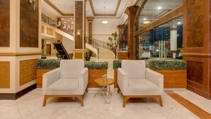 Eine Lobby mit zwei Sesseln, einem kleinen runden Tisch, einer Treppe und einem großen Fenster.