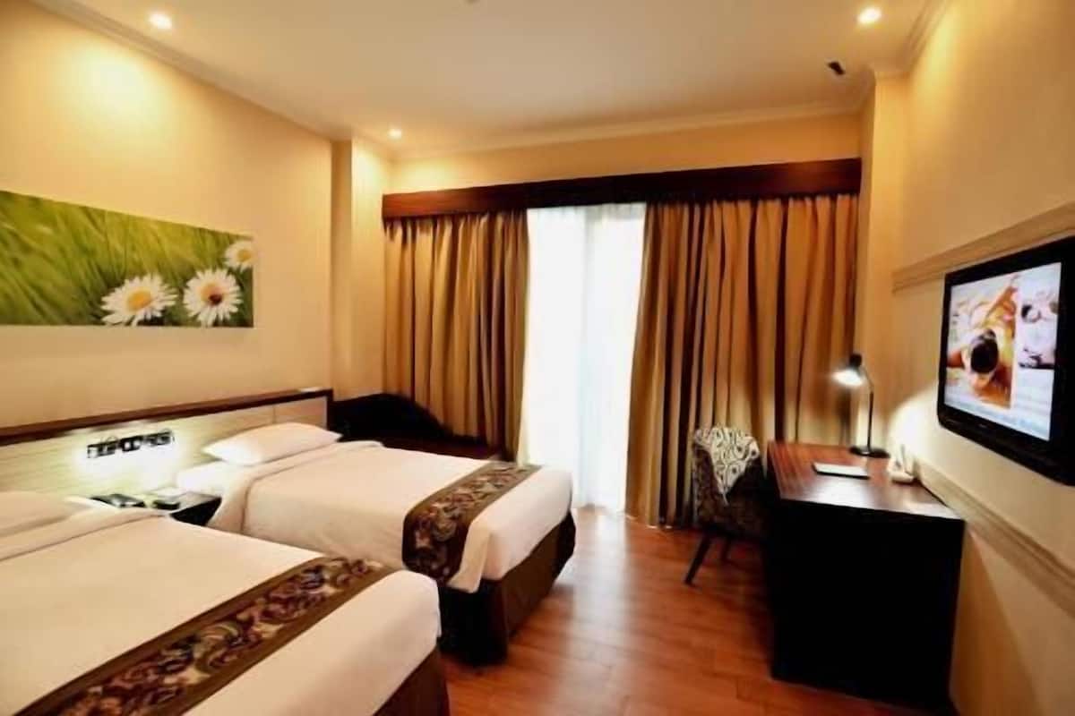 A hotel room with two beds, a desk, a TV, and a window with curtains.