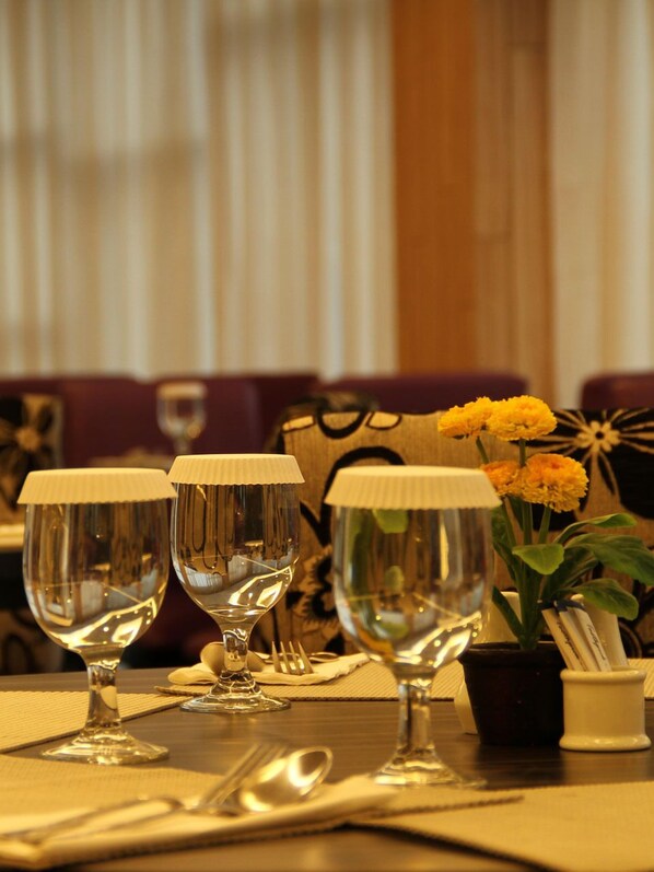 A dining table set with three wine glasses, a potted plant with yellow flowers, and a small white container.