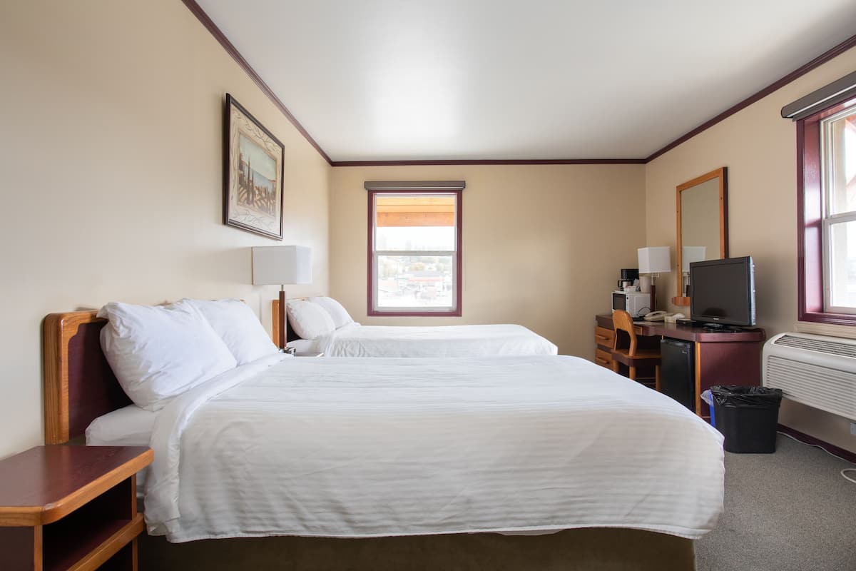 Une chambre d’hôtel avec deux lits, un bureau avec un ordinateur, une télévision et une fenêtre avec des stores.