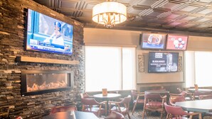 A restaurant with a stone wall, a TV mounted on it, and a chandelier.