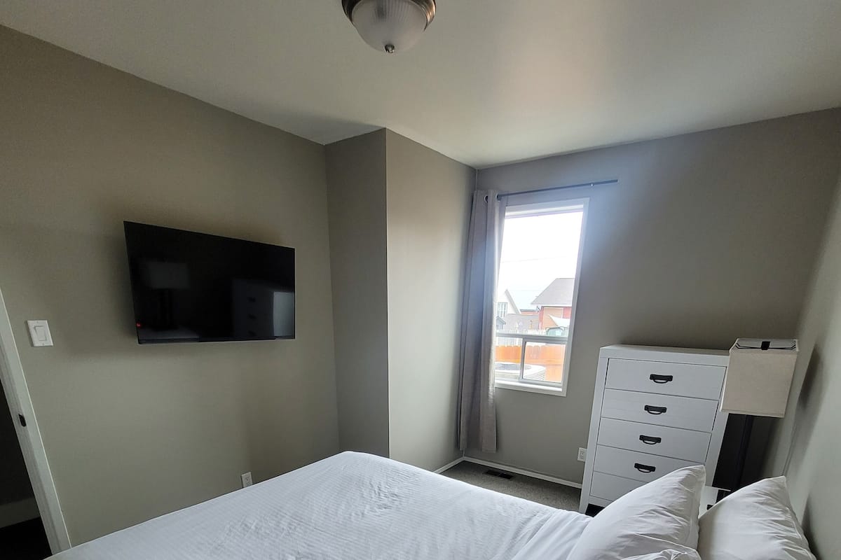 Une chambre d’hôtel avec un lit, un téléviseur fixé au mur, une fenêtre et une commode.