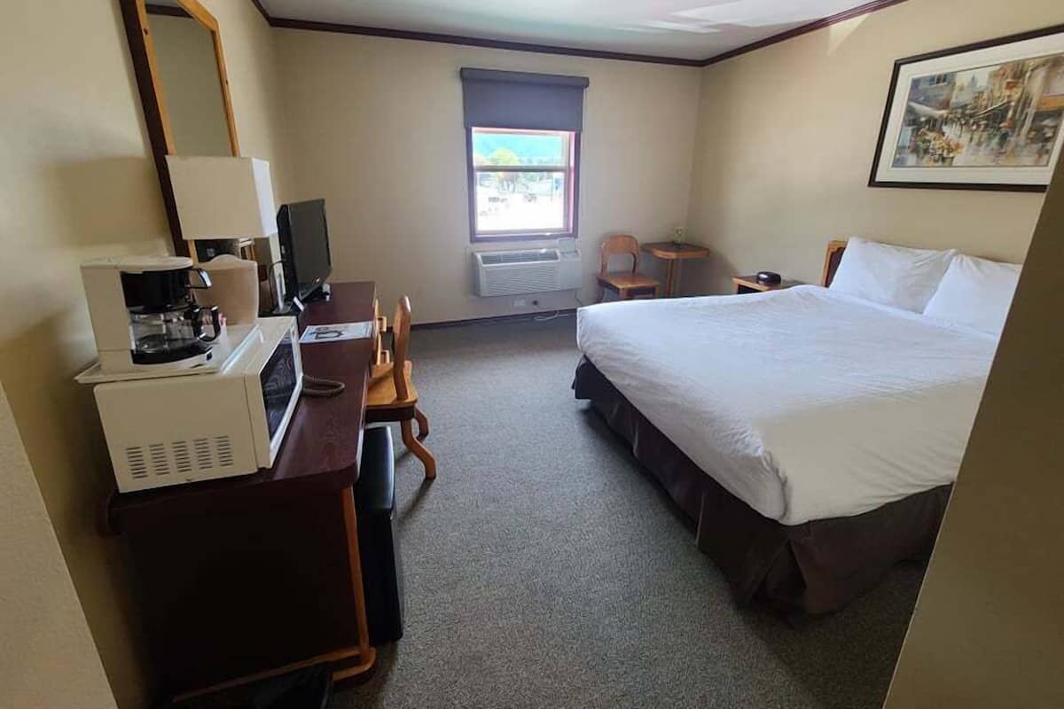 Une chambre d’hôtel comprenant un lit, un bureau avec une machine à café, une chaise, une petite table, une fenêtre avec vue et un tableau encadré au mur.