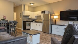 A modern kitchen with white cabinets, stainless steel appliances, and a flat-screen TV.