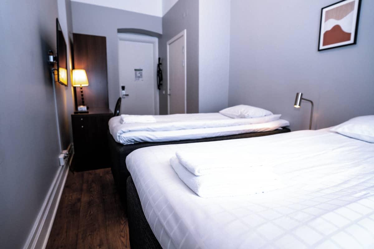 A hotel room with two beds, a nightstand, a lamp, and a door.
