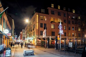 A nighttime street view of Queen's Hotel with a visible sign, a bicycle parked outside, and a pedestrian walkway. - Queen's Hotel by First Hotels (Stockholm)