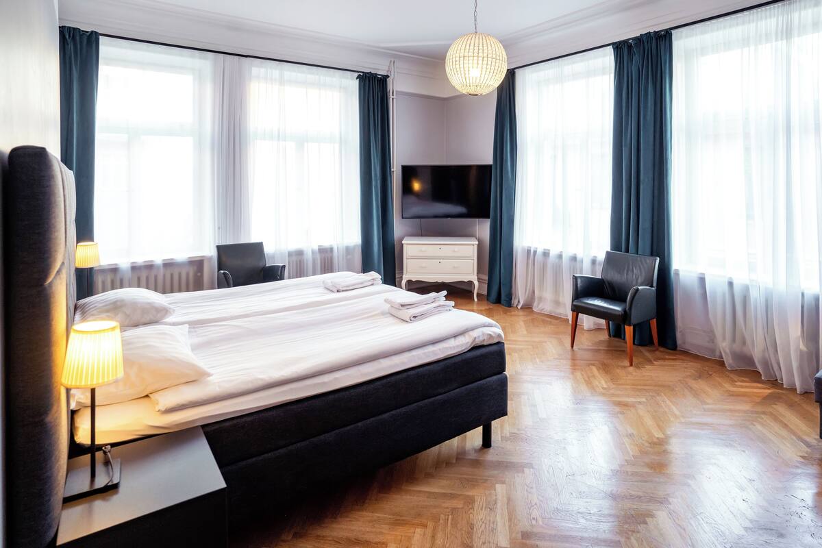A hotel room with a bed, a desk with a lamp, a TV, and a chair.