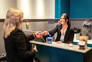A hotel reception desk with a payment terminal, a small candle, and a decorative vase.