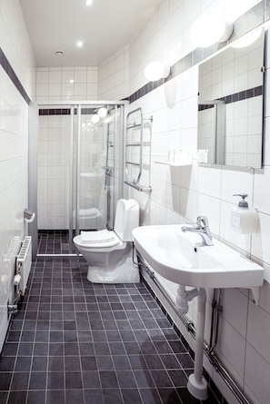 A modern bathroom with a toilet, sink, and glass shower enclosure. - Queen's Hotel by First Hotels (Stockholm)