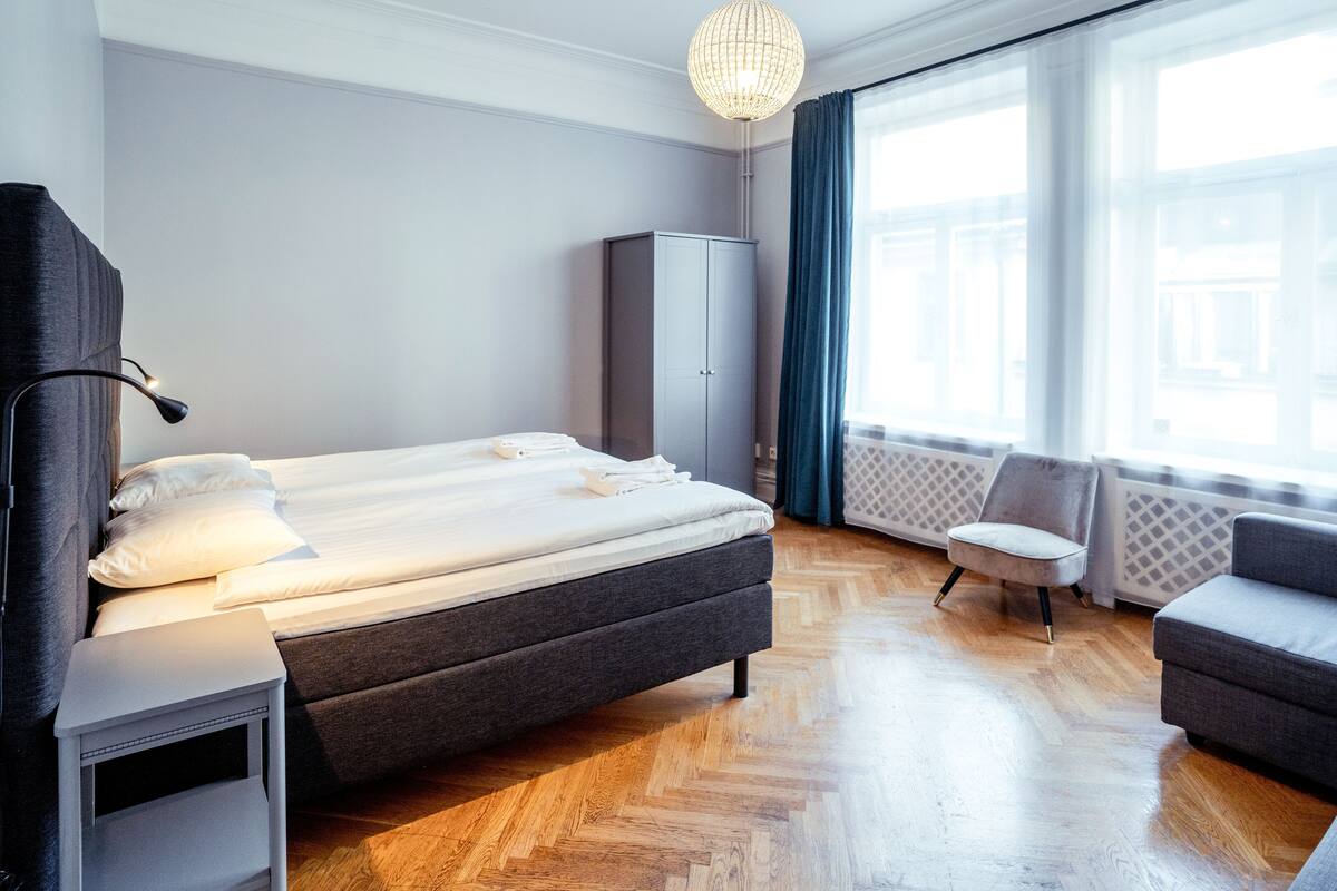 A modern hotel room with a large bed, a wardrobe, a chair, and a sofa.