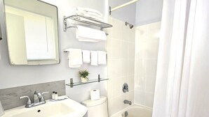 A modern bathroom with a sink, toilet, and bathtub. There is a towel rack above the toilet and a shower curtain. - Lord Nelson Motel (Kingston)