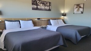 A hotel room with two beds, each with a grey quilted bedspread and white pillows. There is a wall-mounted clock above the beds, and a framed picture of trees on the wall. - Lord Nelson Motel (Kingston)