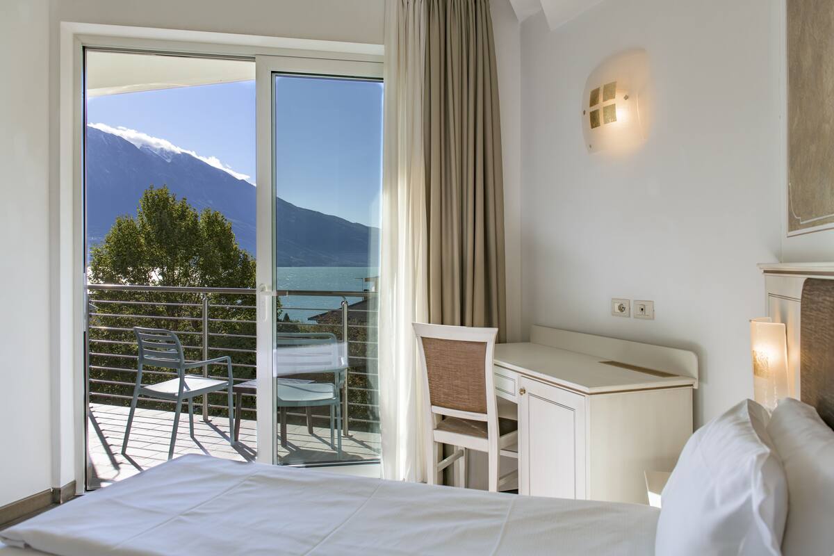 Hotelkamer met een bed, bureau en stoel. Er is een balkon met uitzicht op een berg en een wateroppervlak.