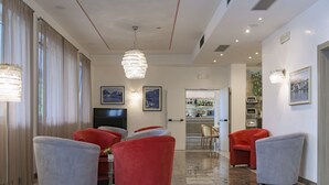 A modern living room with red and grey sofas, a TV, and a bar area in the background. - Hotel Sogno del Benaco (Limone sul Garda)