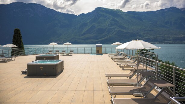 A rooftop terrace with lounge chairs and hot tubs overlooking a lake and mountains. - Hotel Sogno del Benaco (Limone sul Garda)