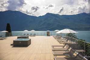 A rooftop terrace with lounge chairs and hot tubs overlooking a lake and mountains. - Hotel Sogno del Benaco (Limone sul Garda)