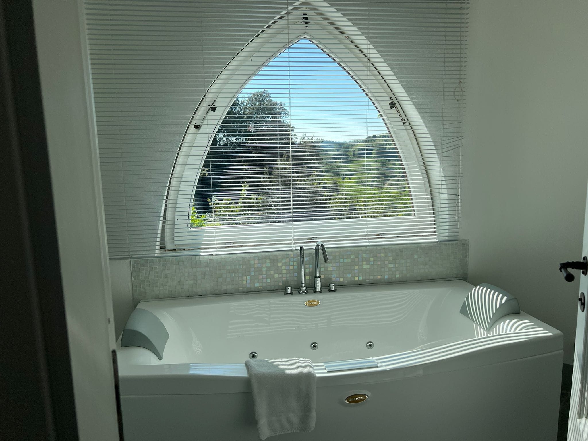 Een moderne badkamer met een vrijstaand bad, een raam met zonwering en een handdoekhouder.