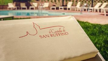 A poolside view with lounge chairs and umbrellas, a pool, and a large building with arched windows in the background.