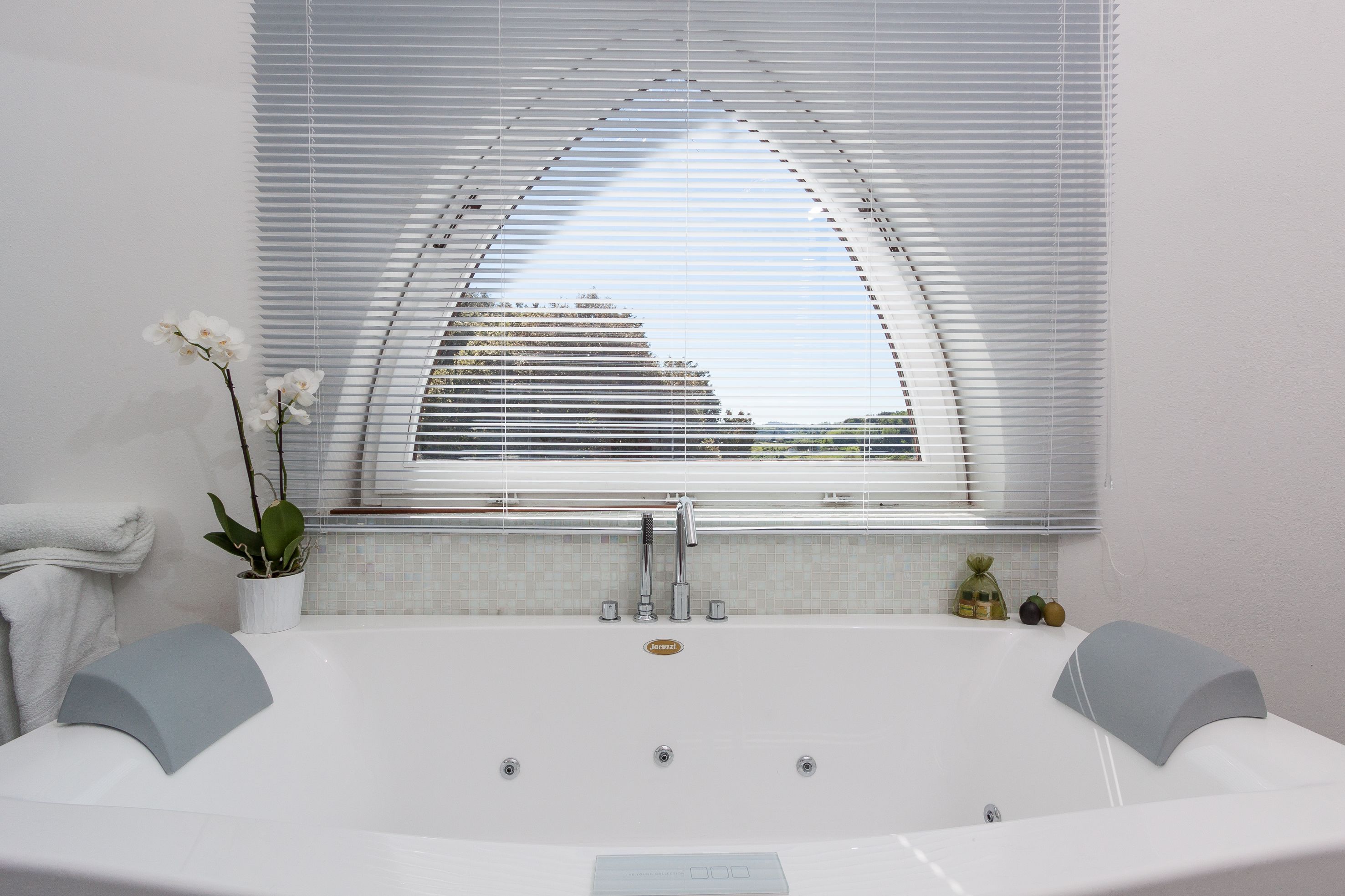 Ein modernes Badezimmer mit einer großzügigen Badewanne, einem Topf-Orchideenstrauch und einem Fenster mit Jalousien.