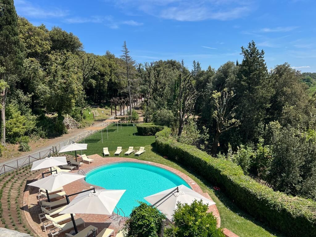 Ein Swimmingpool mit Liegestühlen und Sonnenschirmen, umgeben von einem gepflegten Garten und Bäumen.