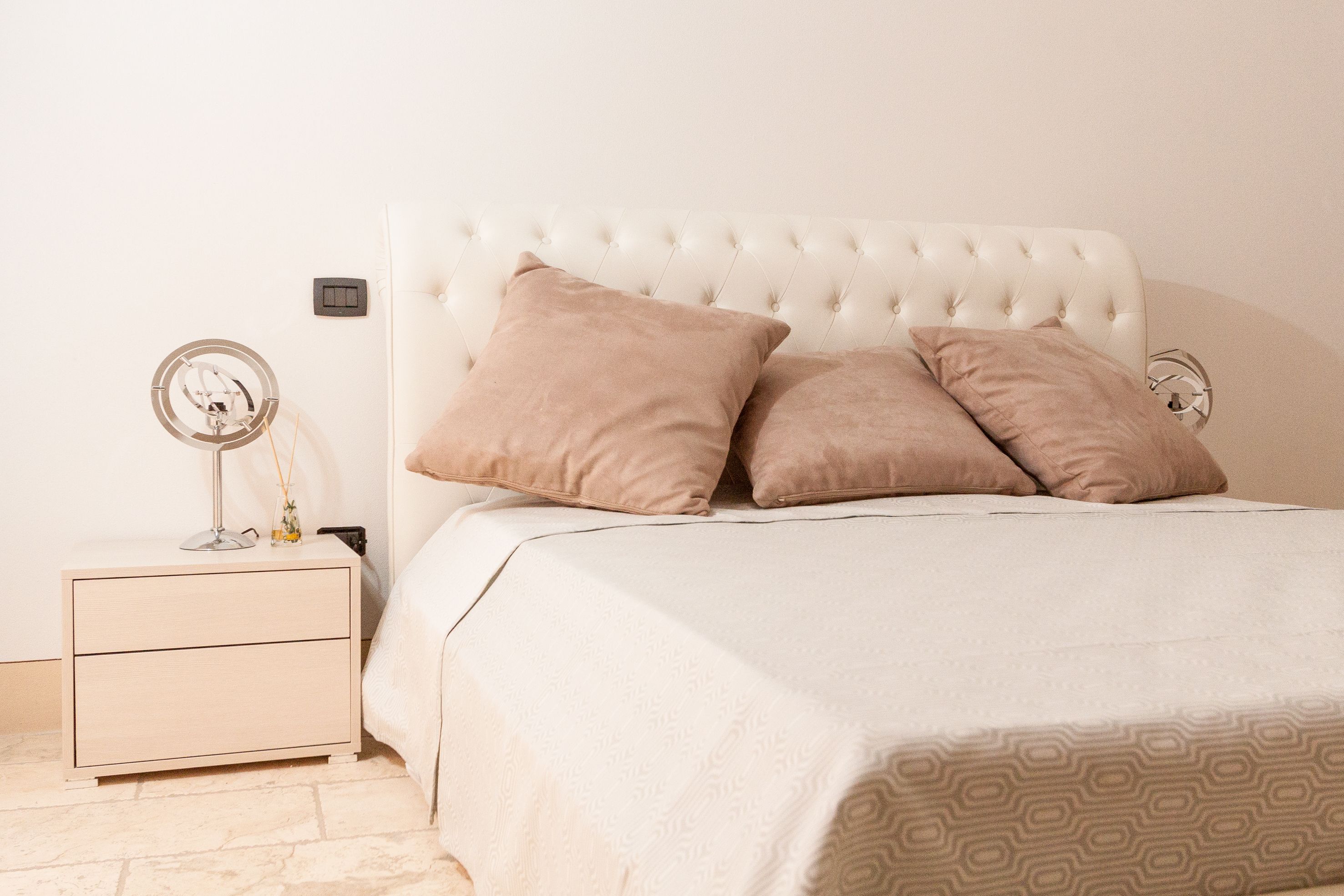 A bedroom with a tufted headboard, two bedside tables, a bed with a patterned bedspread, and a small bedside lamp.