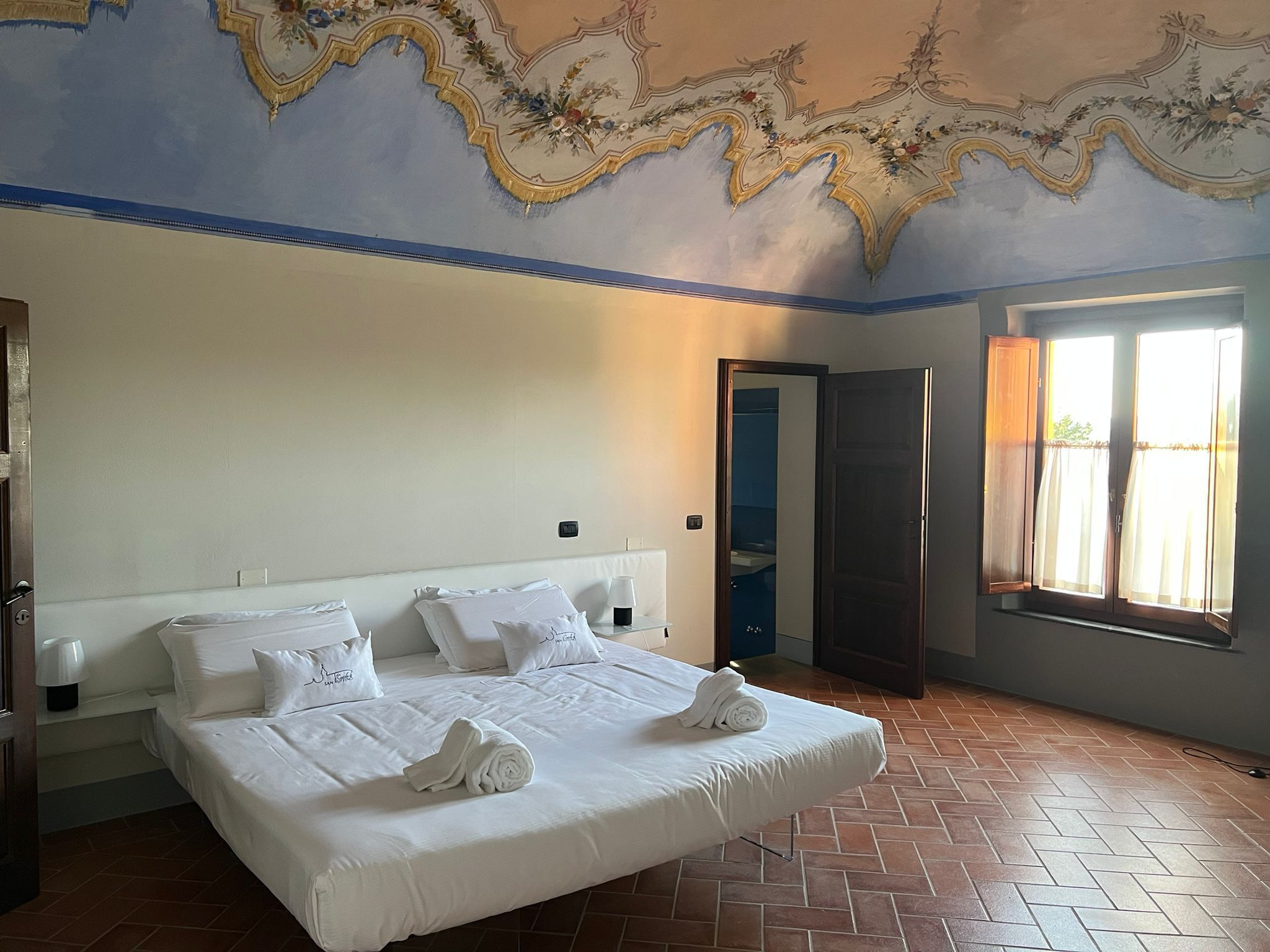 Quarto de hotel com uma cama grande, um guarda-roupa e uma janela com cortinas.