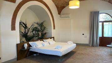 A hotel room with a bed, a potted plant, a hanging light fixture, and a window with curtains.