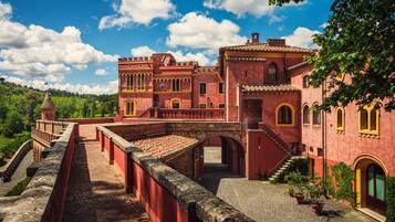 Un edificio histórico con fachada roja, un puente y montañas al fondo.